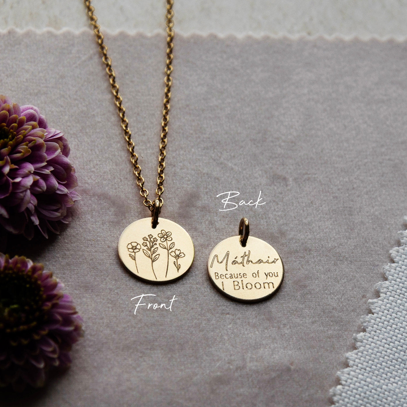 Flatlay of the Mathair Bloom Necklace on soft pink velvet fabric, showing the front and back engravings side by side.