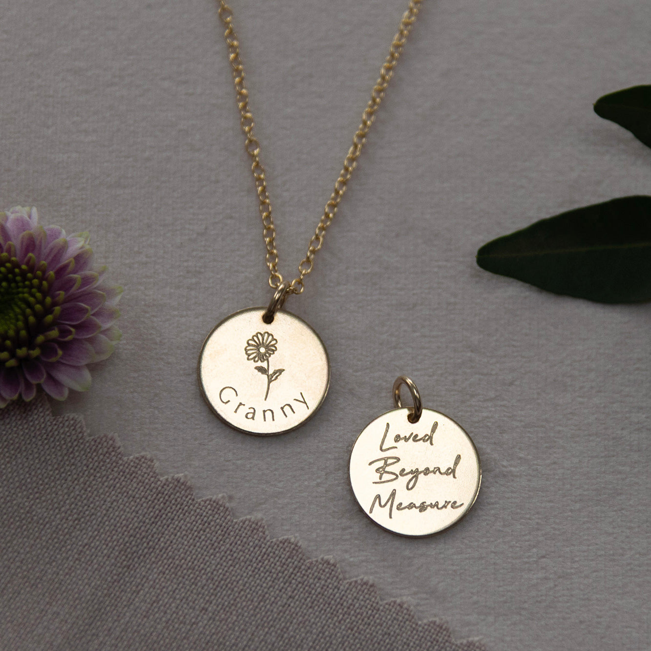Front and back of the personalised grandmother necklace shown side by side in a flatlay with flowers.