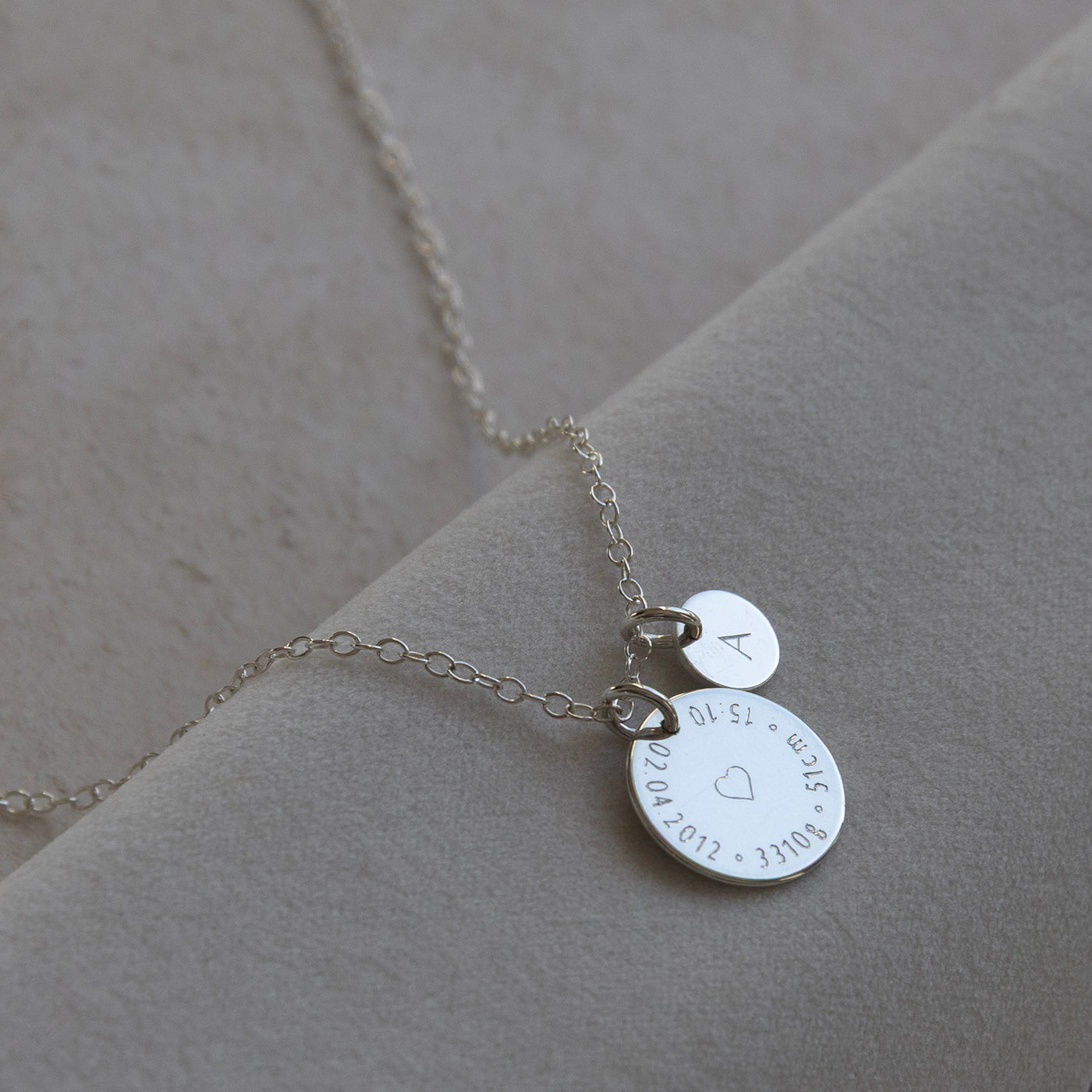Detailed view of sterling silver Birthcoin necklace with baby’s birth date, time, weight and height engraved around a heart – custom birth keepsake.