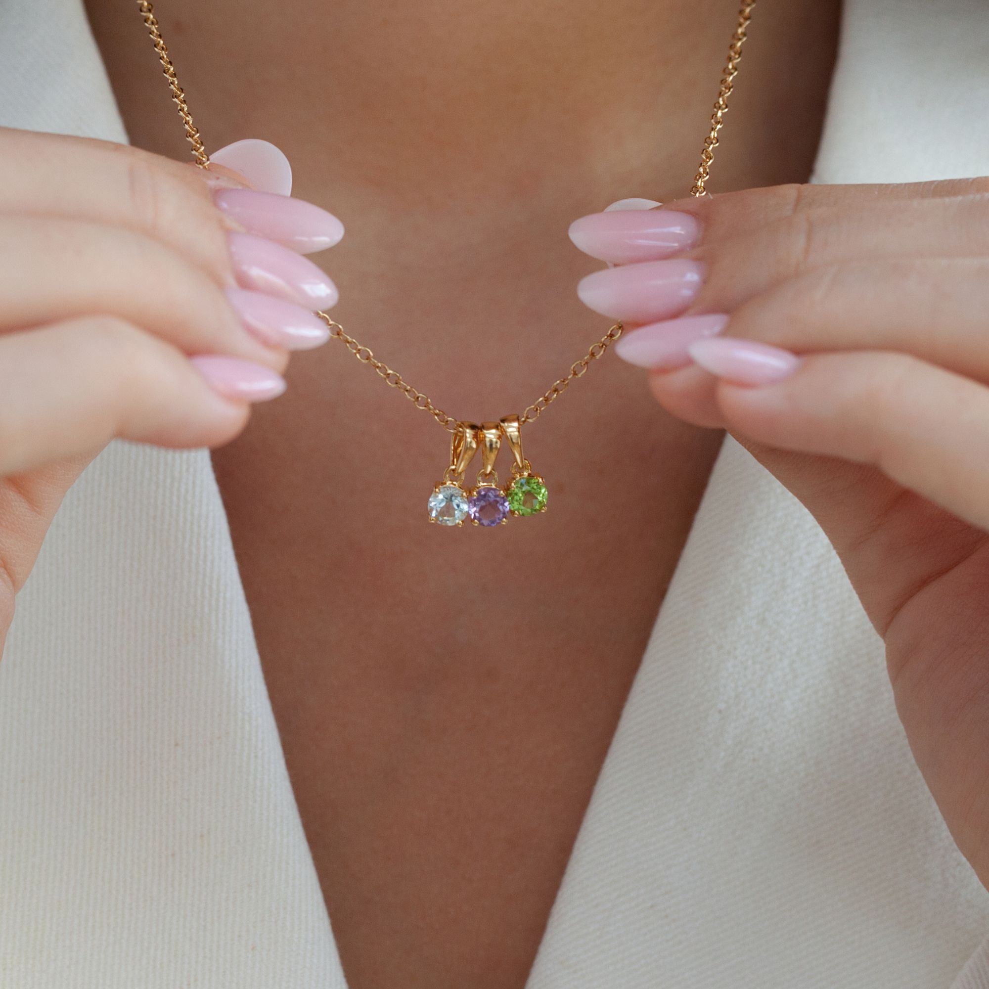Three dainty gold birthstone pendants – aquamarine, amethyst and peridot – on a gold chain held by a model