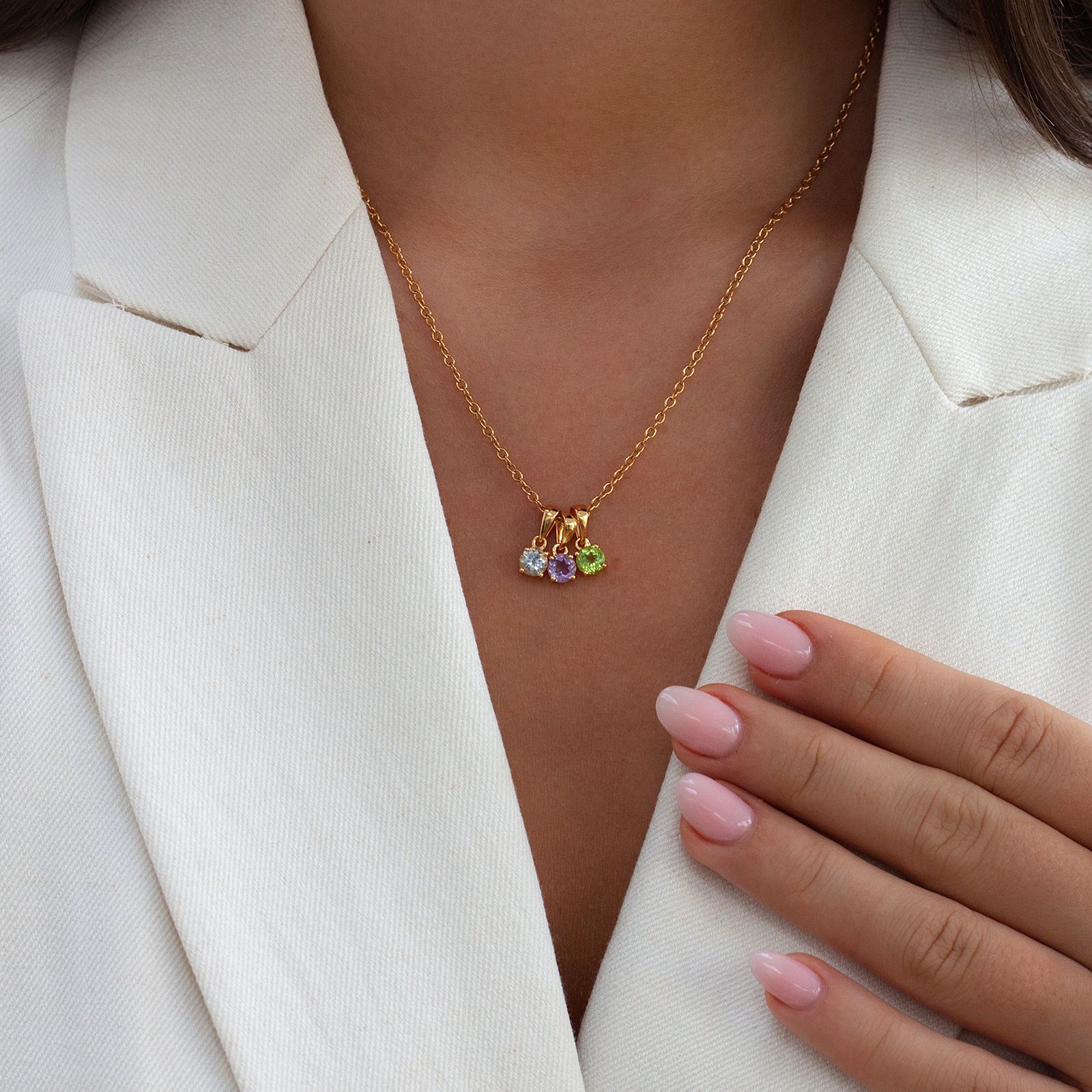 Three dainty gold birthstone pendants – aquamarine, amethyst and peridot – worn together on a gold chain by a model