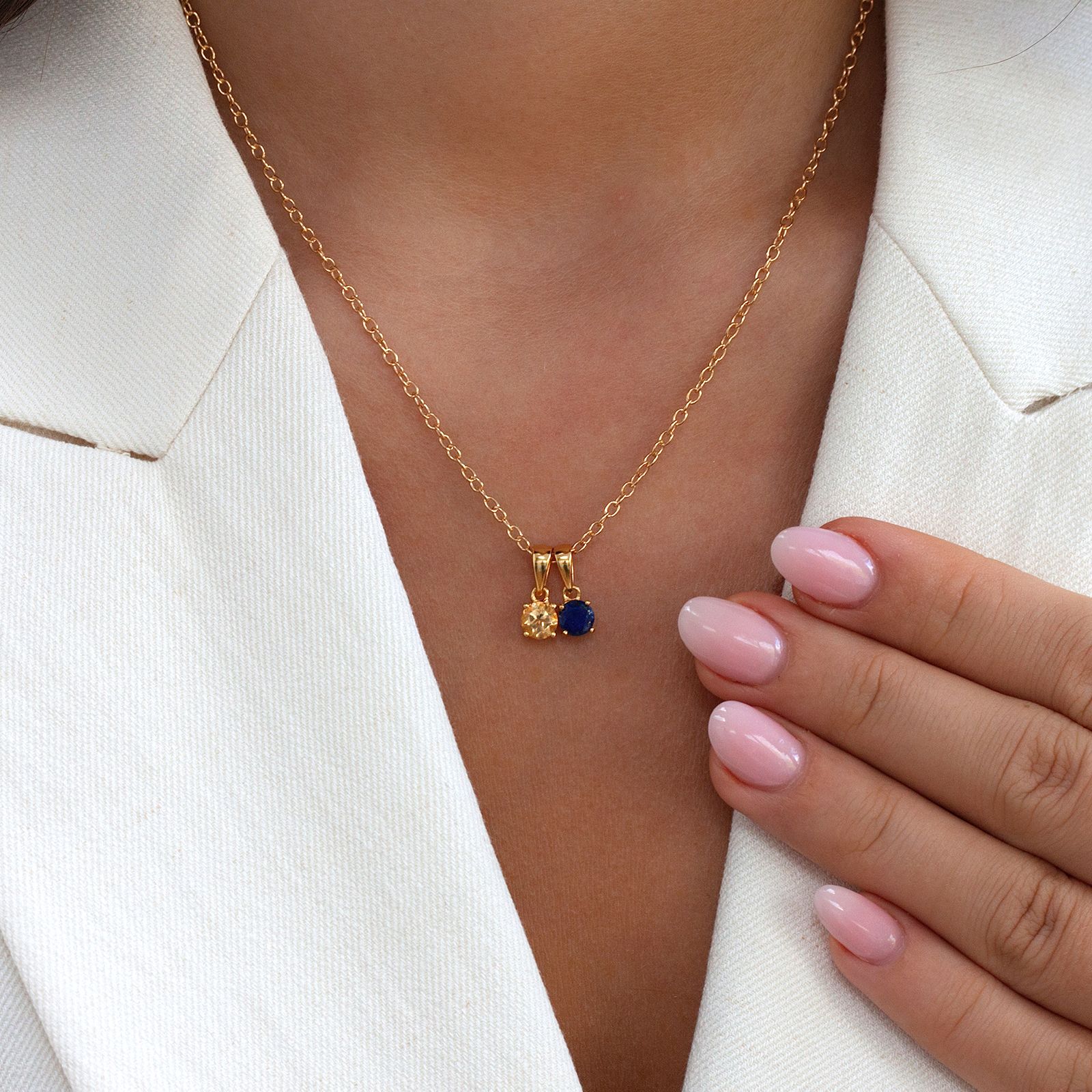 Two dainty gold birthstone pendants – citrine and lapis lazuli – worn together on a gold chain by a model