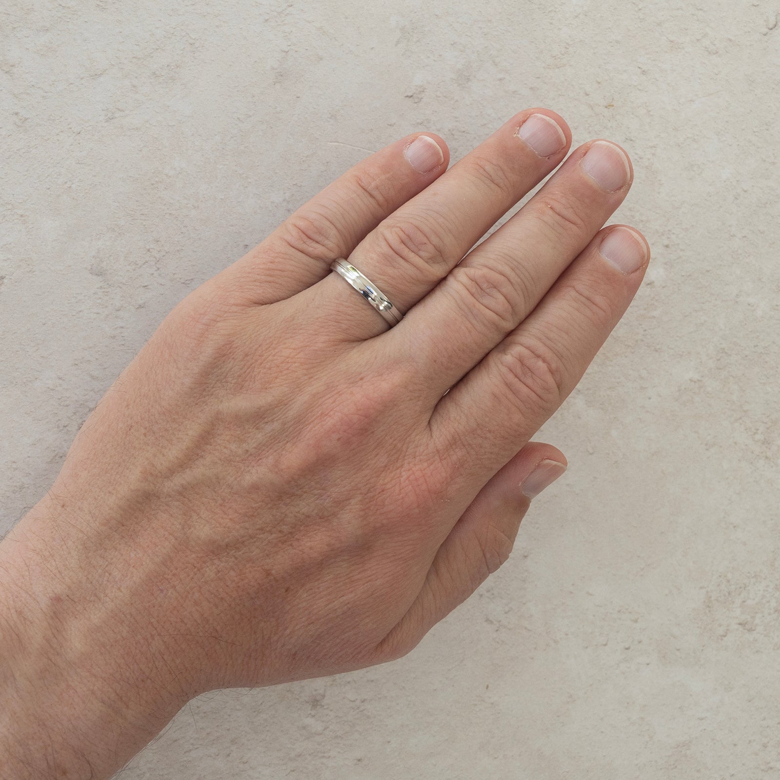 The One Path wedding ring worn on a model's hand — a 4mm men's ring with a single groove running around the middle