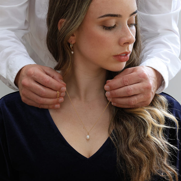 Partner fastening a pearl pendant necklace for her